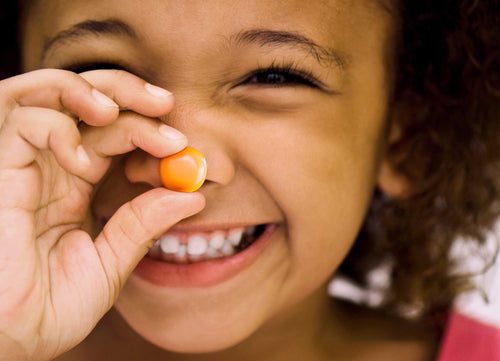 Child holding a small orange object near their eye