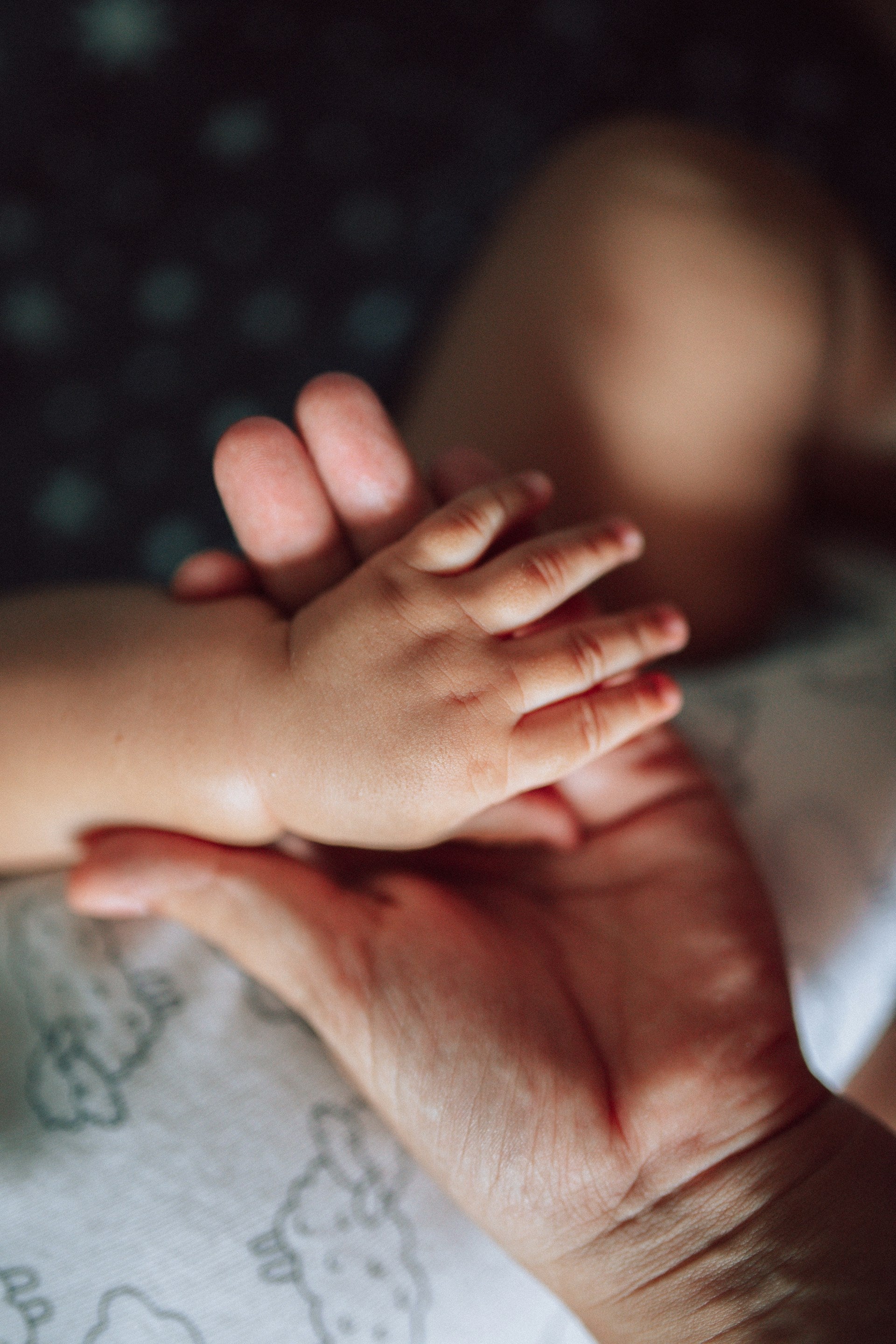 Close-up of an adult hand holding a child's hand, with a blurred background